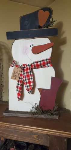 a snowman with a hat and scarf on top of a wooden shelf next to christmas decorations