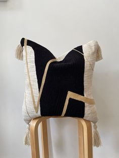 a black and white pillow with tassels sitting on a wooden chair next to a wall