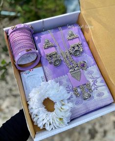 an open box with jewelry and flowers on the ground next to some thread, scissors and other items