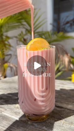 a pink drink being poured into a glass with an orange slice in it on a wooden table