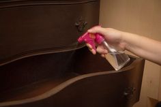 a person using a spray bottle to clean an old dresser with pink handles and knobs