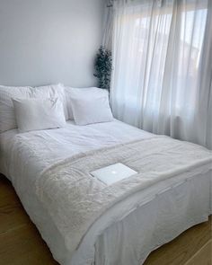 a bed with white sheets and pillows in front of a window, next to a laptop computer