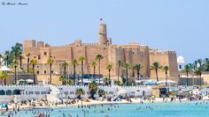 people are swimming in the water near an old building and palm trees on the beach