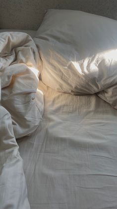 an unmade bed with white sheets and pillows