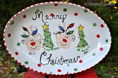 a merry christmas plate sitting on top of a wooden table next to some trees and bushes