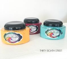 three jars of body scrubs sitting next to each other on a white counter top