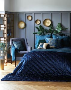 a bed with blue comforter and pillows in a bedroom next to a plant on the wall