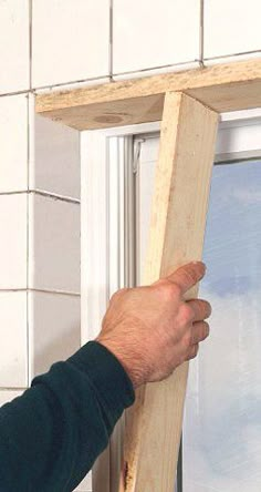 a man is holding up a window frame to the side of his house with one hand