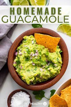 a wooden bowl filled with guacamole surrounded by tortilla chips and lime wedges