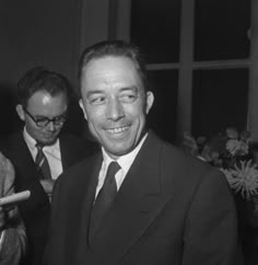 black and white photograph of two men in suits looking at something on the table while another man smiles