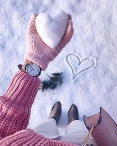 two people standing in the snow with their feet up and holding a heart shaped clock