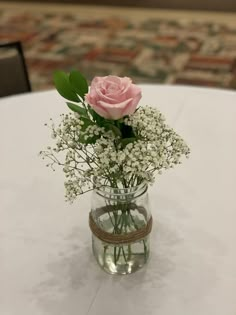 a pink rose in a glass vase with baby's breath tied to it on a table