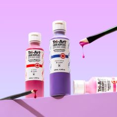 two bottles of acrylic paint and a brush on a purple shelf with pink background