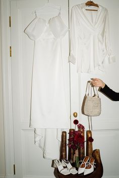 a woman holding a purse next to a white dress hanging on a rack with shoes and handbags