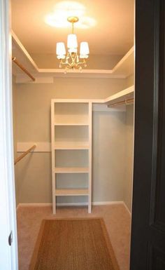 an empty walk in closet next to a door with a chandelier hanging from the ceiling