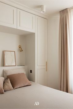 a bedroom with white walls and beige pillows on the bed, next to a window