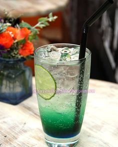 a green and blue drink sitting on top of a wooden table next to an orange flower