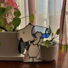 a glass sculpture of a dog drinking from a cup on top of a table next to a potted plant