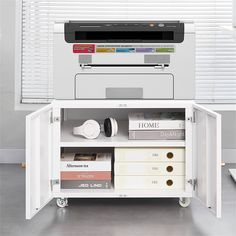 a printer sitting on top of a white cabinet next to some books and other items