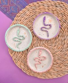 three small bowls with designs on them sitting on a wicker table top next to a purple and blue rug