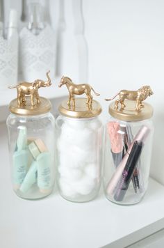 three jars filled with different types of items on top of a white counter topped with gold horse figurines