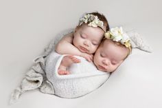 two babies are sleeping together on a white blanket with flowers in their hair and one is wearing a flower headband