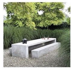 a concrete bench sitting in the middle of a gravel field next to tall grass and trees