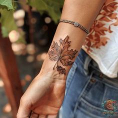 a woman's arm with a leaf tattoo on the left side of her wrist