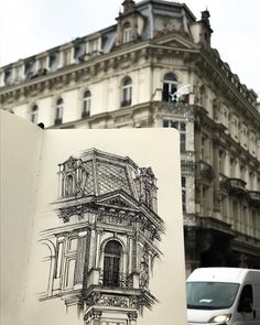 an open book with a drawing on it in front of a large building and cars