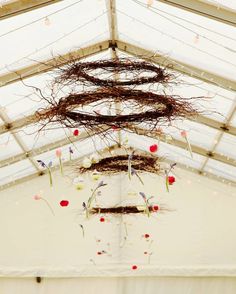 an arrangement of branches and flowers hanging from the ceiling in a white tented area