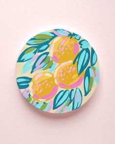 a plate with fruit painted on it sitting on a pink surface, next to a white wall