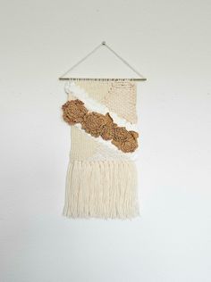 a white wall hanging with brown flowers and fringes on it's side, in front of a white wall