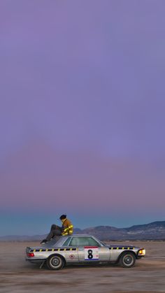 two men sitting on top of a car in the desert