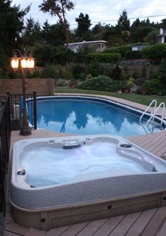 a hot tub sitting on top of a wooden deck next to a swimming pool in the middle of a yard