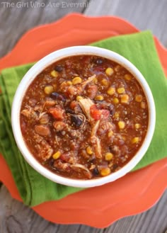 a white bowl filled with chili and corn on top of a green napkin next to an orange plate