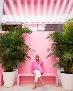 a woman sitting on a pink bench next to two potted plants and wearing sunglasses