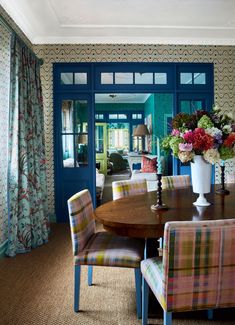 a dining room table with colorful chairs and flowers in vases on the end tables