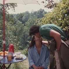 a man kissing a woman on the cheek in front of an outdoor table with drinks