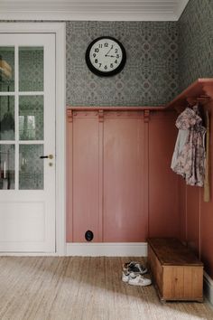 a room with pink walls and a clock on the wall next to a wooden bench