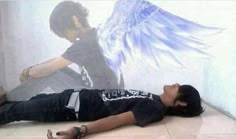 a young man laying on the floor with an angel painted on the wall behind him