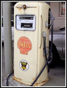 an old yellow shell gas pump sitting next to a car