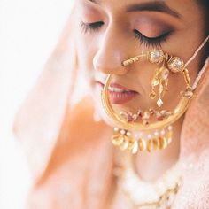 a close up of a woman wearing gold jewelry and earrings with her eyes closed to the camera