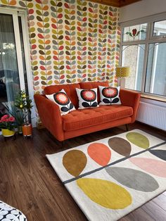 an orange couch sitting in front of a window on top of a hard wood floor