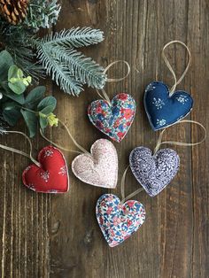 four heart ornaments hanging from twine on a wooden table next to evergreen branches and pine cones