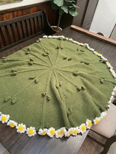 a green blanket with white and yellow flowers sitting on top of a wooden table next to a potted plant