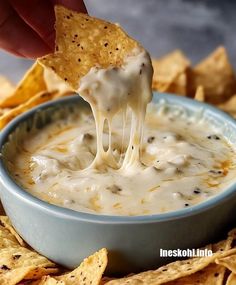 a hand holding a tortilla chip over a bowl of cheese dip with chips