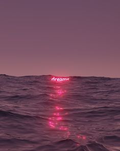 the words dream are lit up in pink light on top of an ocean wave at night