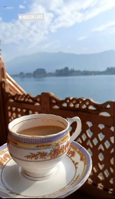 a cup of coffee sitting on top of a saucer next to a balcony overlooking the ocean