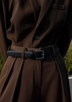 a person wearing a brown trench coat and black pants with a belt around their waist