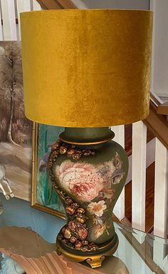 a lamp sitting on top of a glass table next to a framed painting and stairs